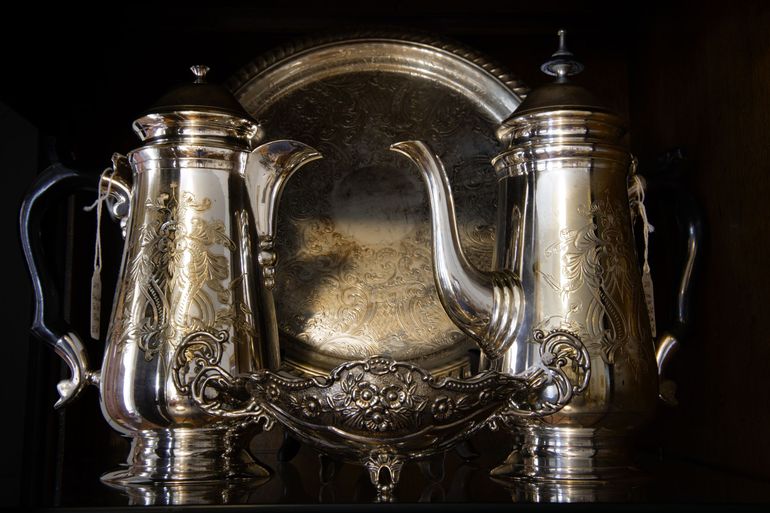 Two silver teapots flanking a large ornate silver tray on a dark background