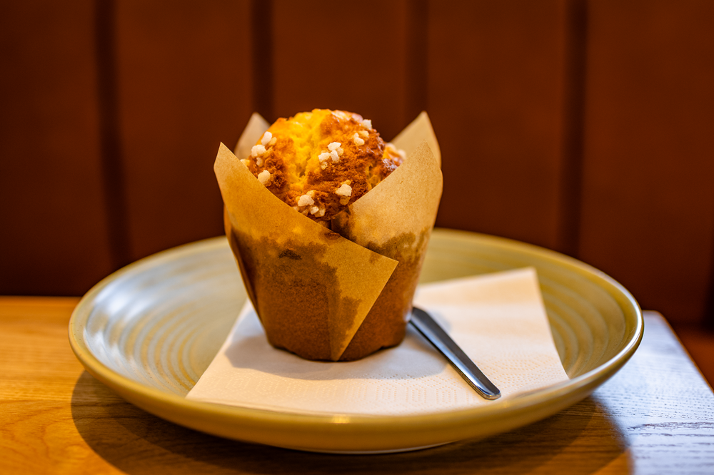 Muffin in paper wrapper on a plate with a napkin and spoon, set on a wooden surface.