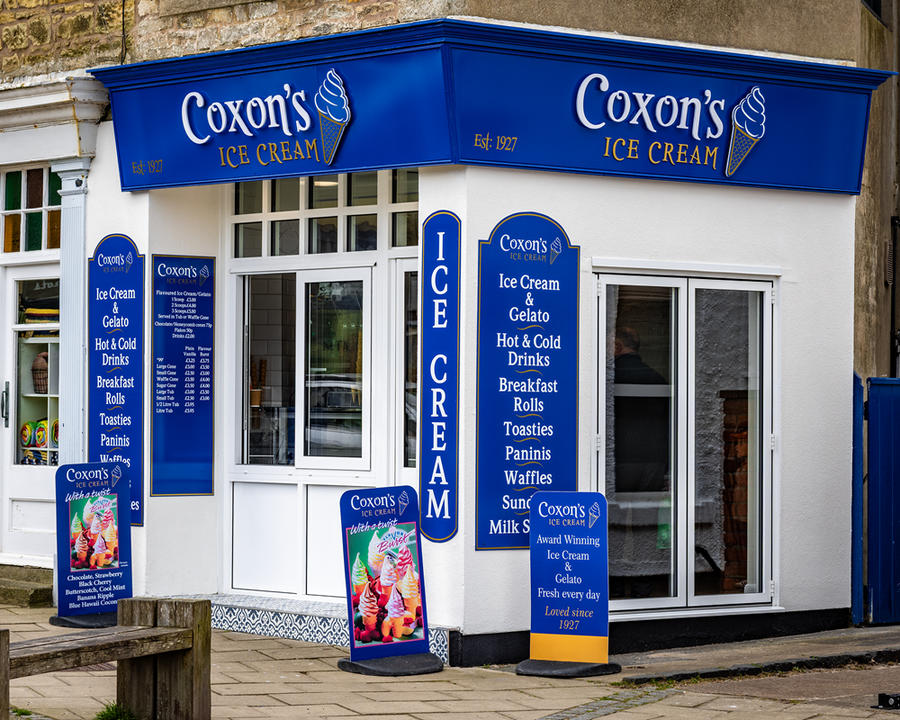 Coxon's Ice Cream shop with blue and white signage. Offers ice cream, breakfast items, and drinks.