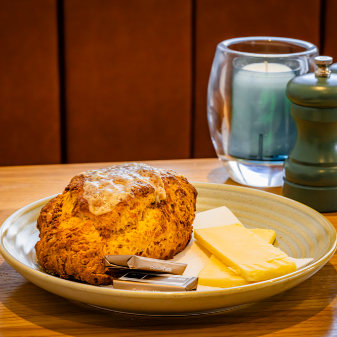 Scone with butter on a plate, candle in glass, and pepper grinder on a wooden table.
