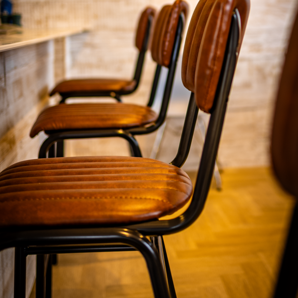 Brown leather bar stools with black metal frames lined up at a counter.