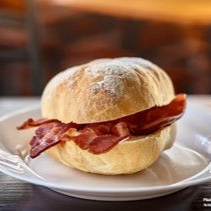 Bacon sandwich on a white plate. Crispy bacon inside a soft, round bun.
