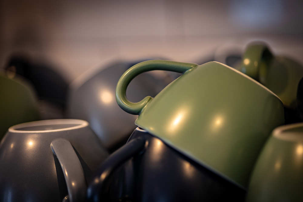 Stacked mugs, mostly gray and green, in a dimly lit setting.