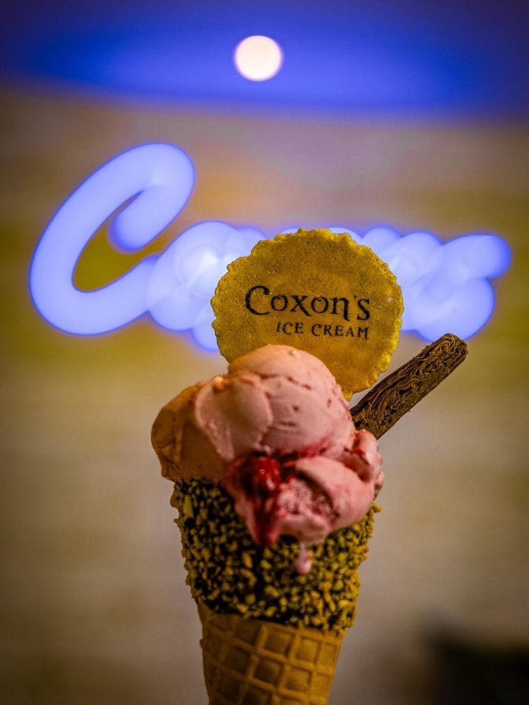 Ice cream cone with pink scoops, cookie, and Coxon's Ice Cream sign in the background.