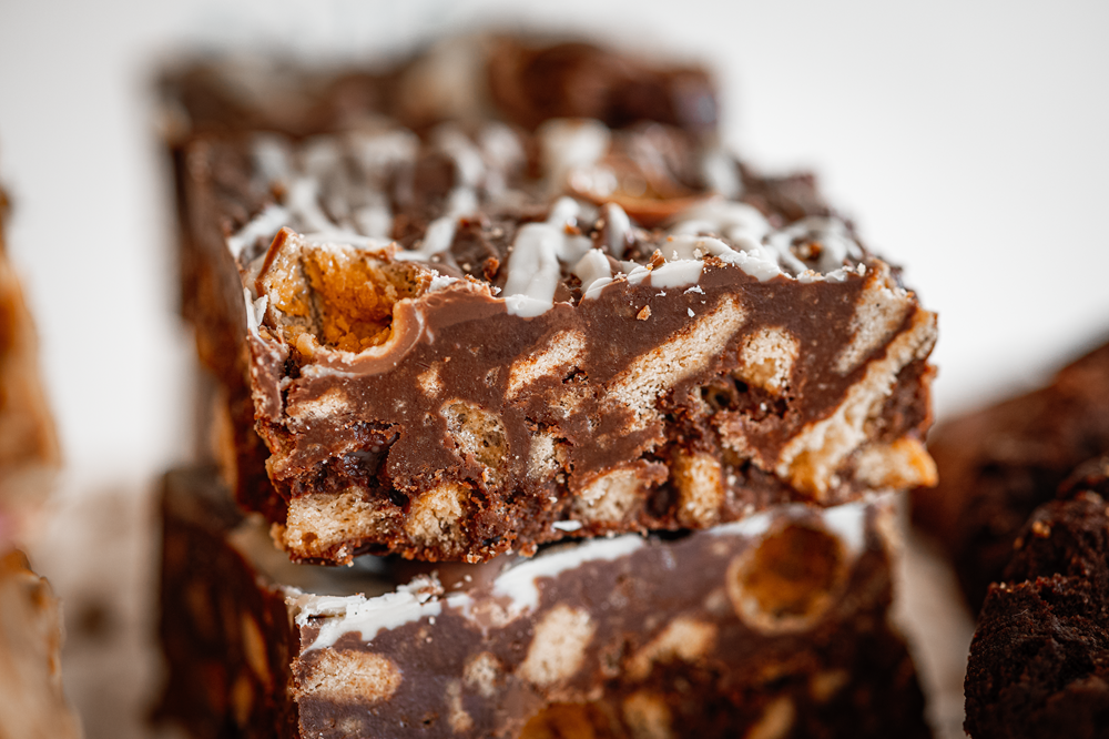 Close-up of stacked chocolate biscuit cake squares with white drizzle.