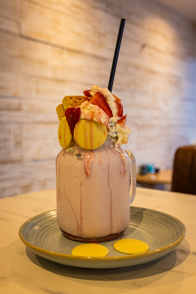 Pink milkshake with toppings, including strawberries, cookies, and macarons, in a mason jar.