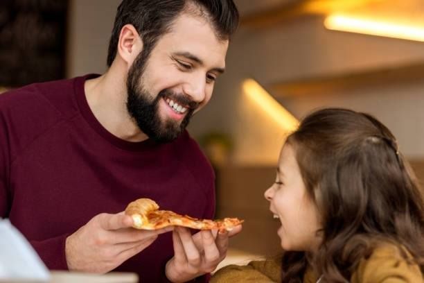 A man and a little girl are eating pizza together.
