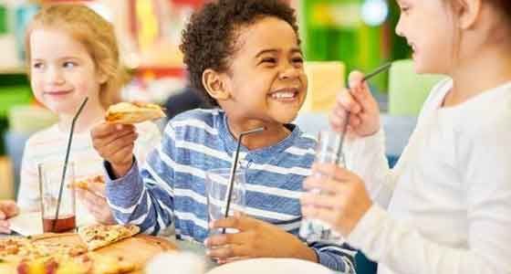 A group of children are sitting at a table eating pizza.