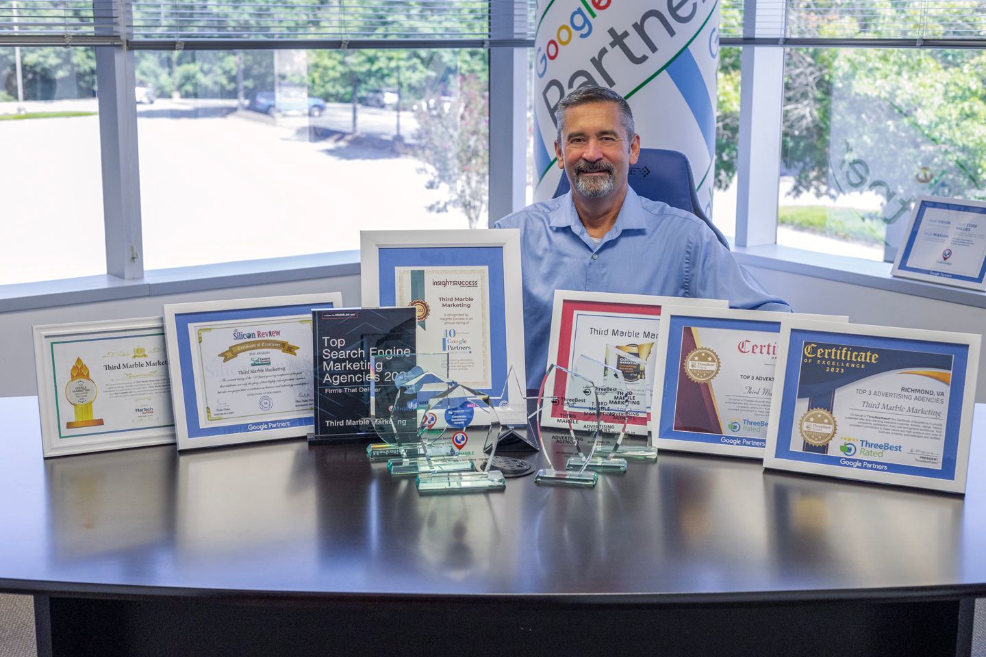 Basic SEO Package: Man seated behind a table displaying framed certificates and awards in a bright office setting