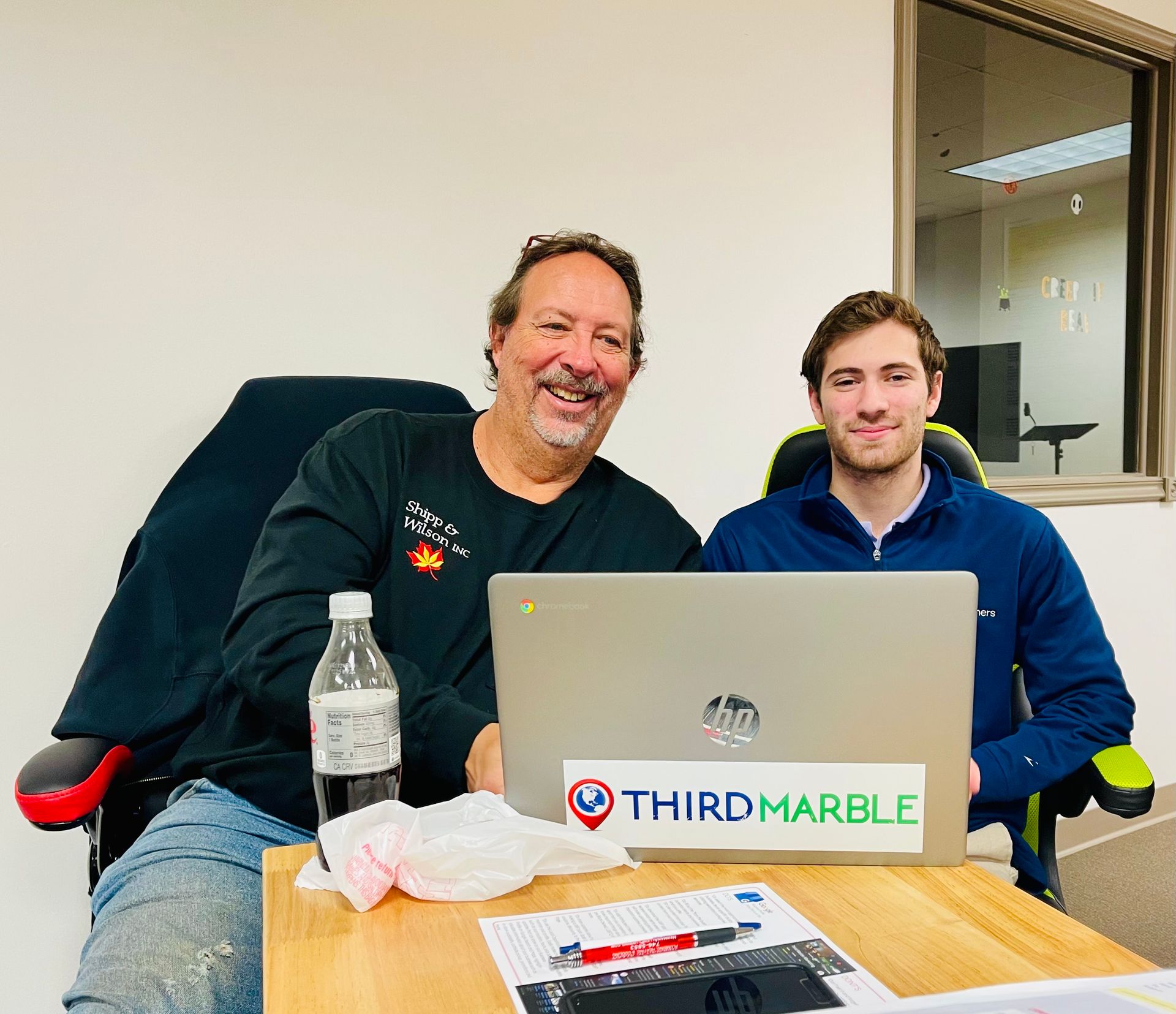 Basic SEO Package: Two people seated at a table behind a laptop in an office, smiling at the camera.