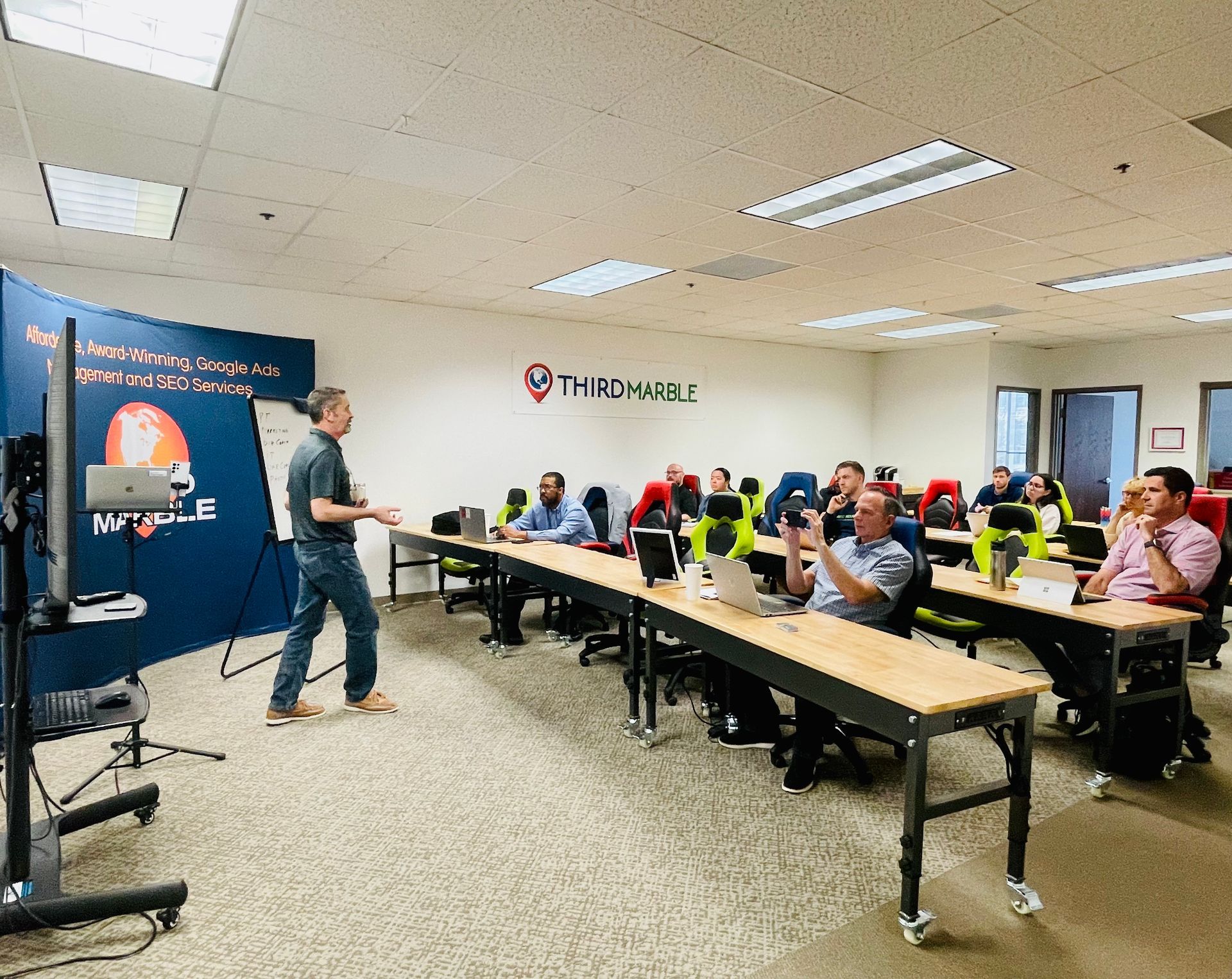 Basic SEO Package: Instructor speaking to seated attendees in a classroom with tables and a presentation screen