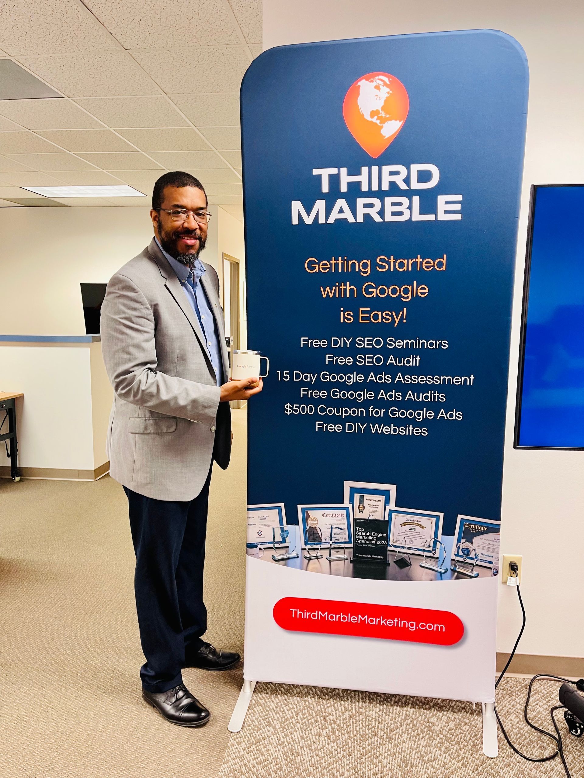 Basic SEO Package: Man standing beside a blue Third Marble promotional banner at a trade show booth