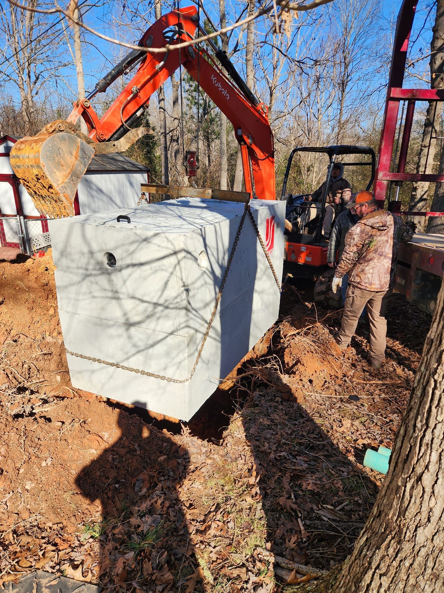 A man is standing next to a large concrete block being lifted by an excavator.