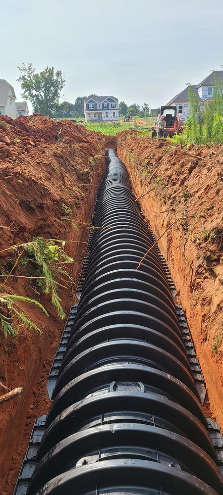 A large black pipe is being installed in a trench.