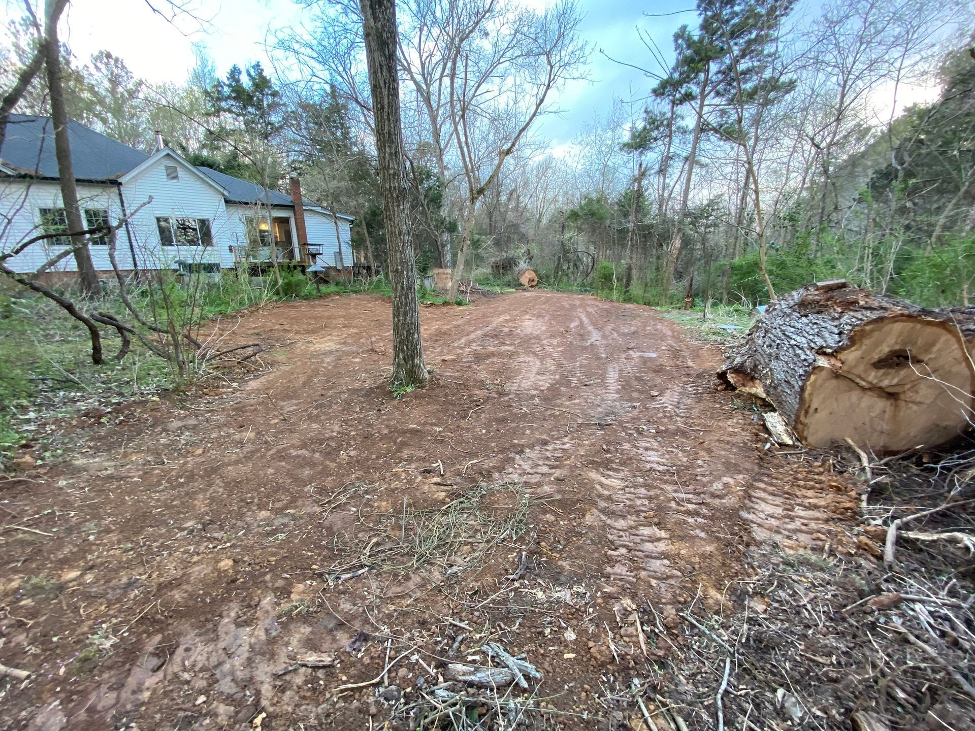 A large log is sitting in the middle of a dirt road in front of a house.