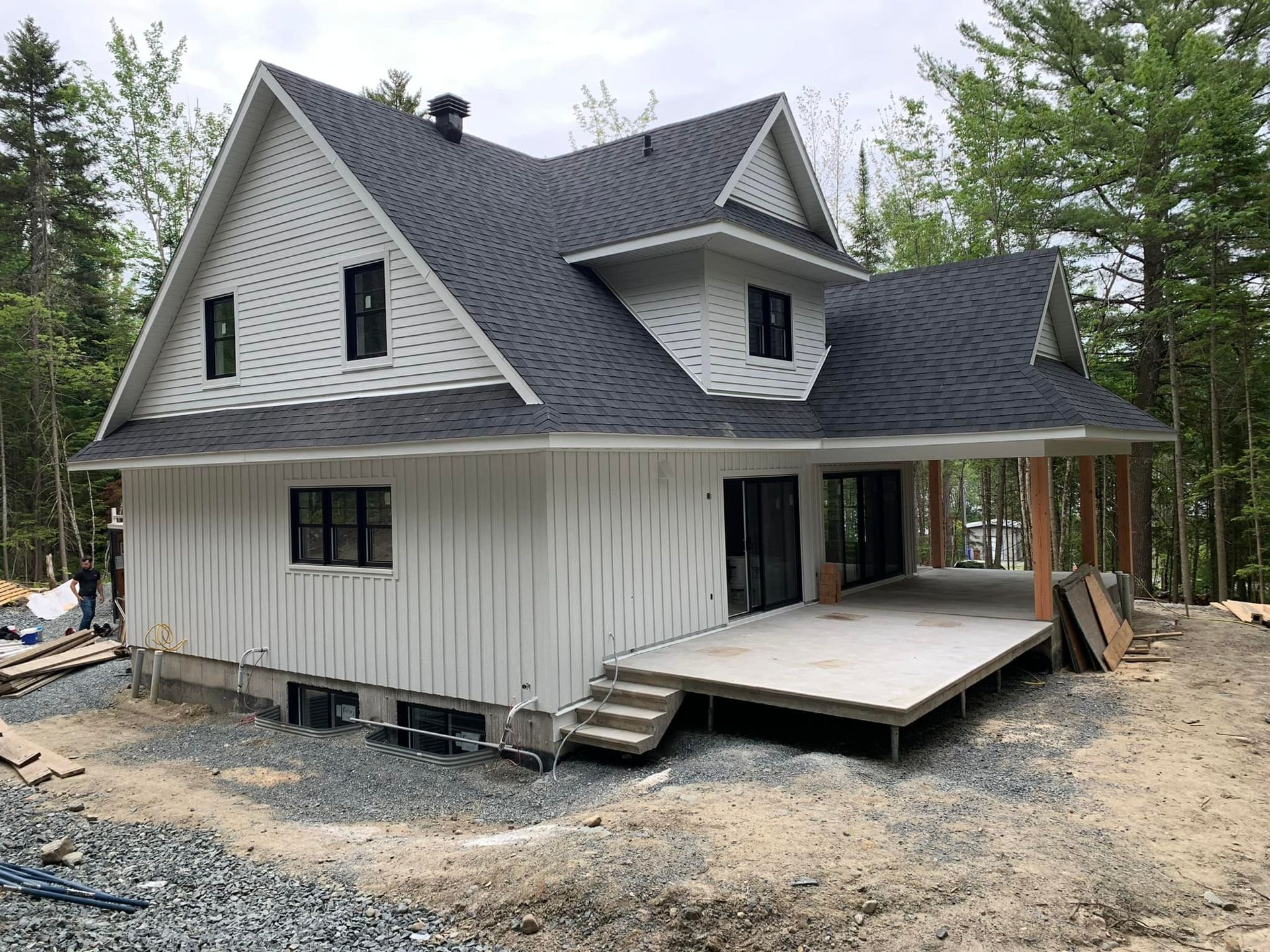 Une maison blanche avec un toit noir est en construction dans les bois.
