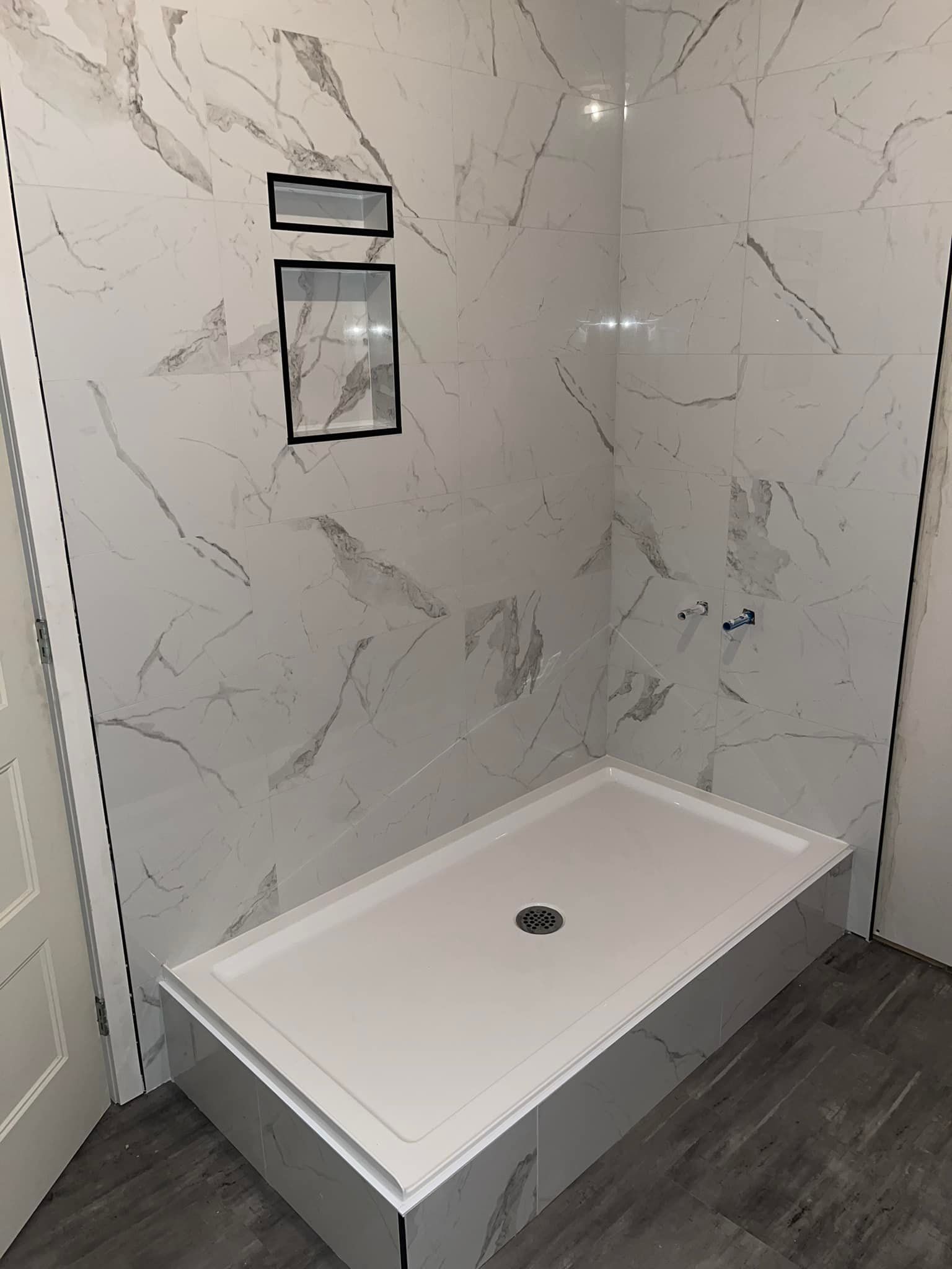 Une cabine de douche dans une salle de bain aux murs en marbre.