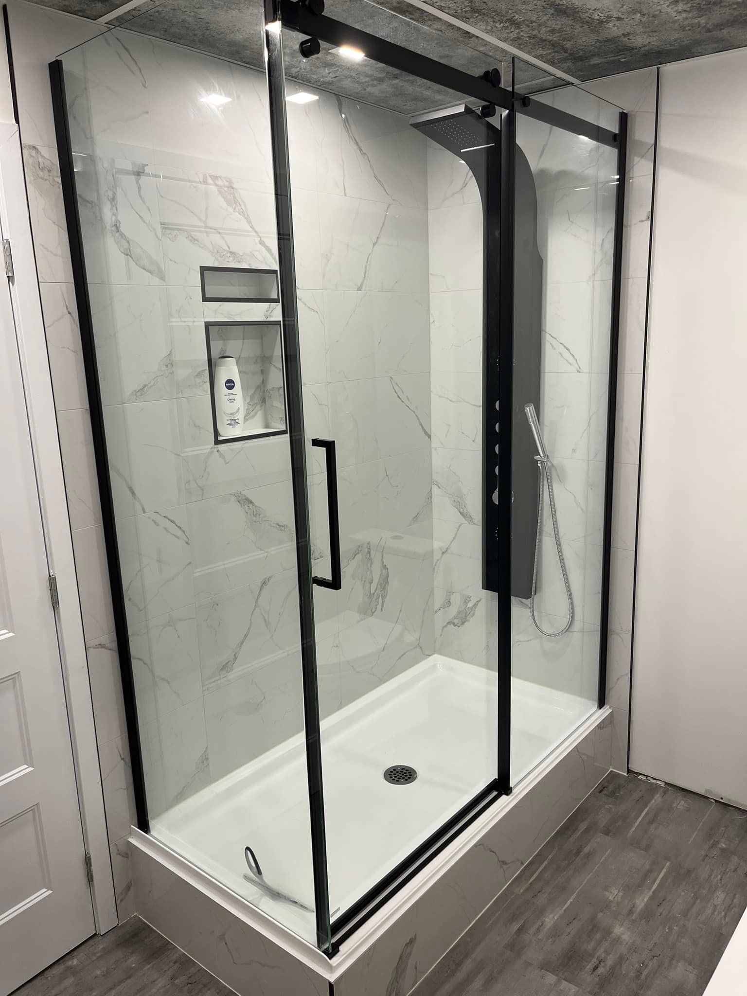 Une cabine de douche avec un cadre noir et des portes coulissantes en verre dans une salle de bain.