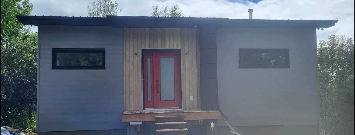 Une petite maison blanche avec une porte rouge et un porche en bois.