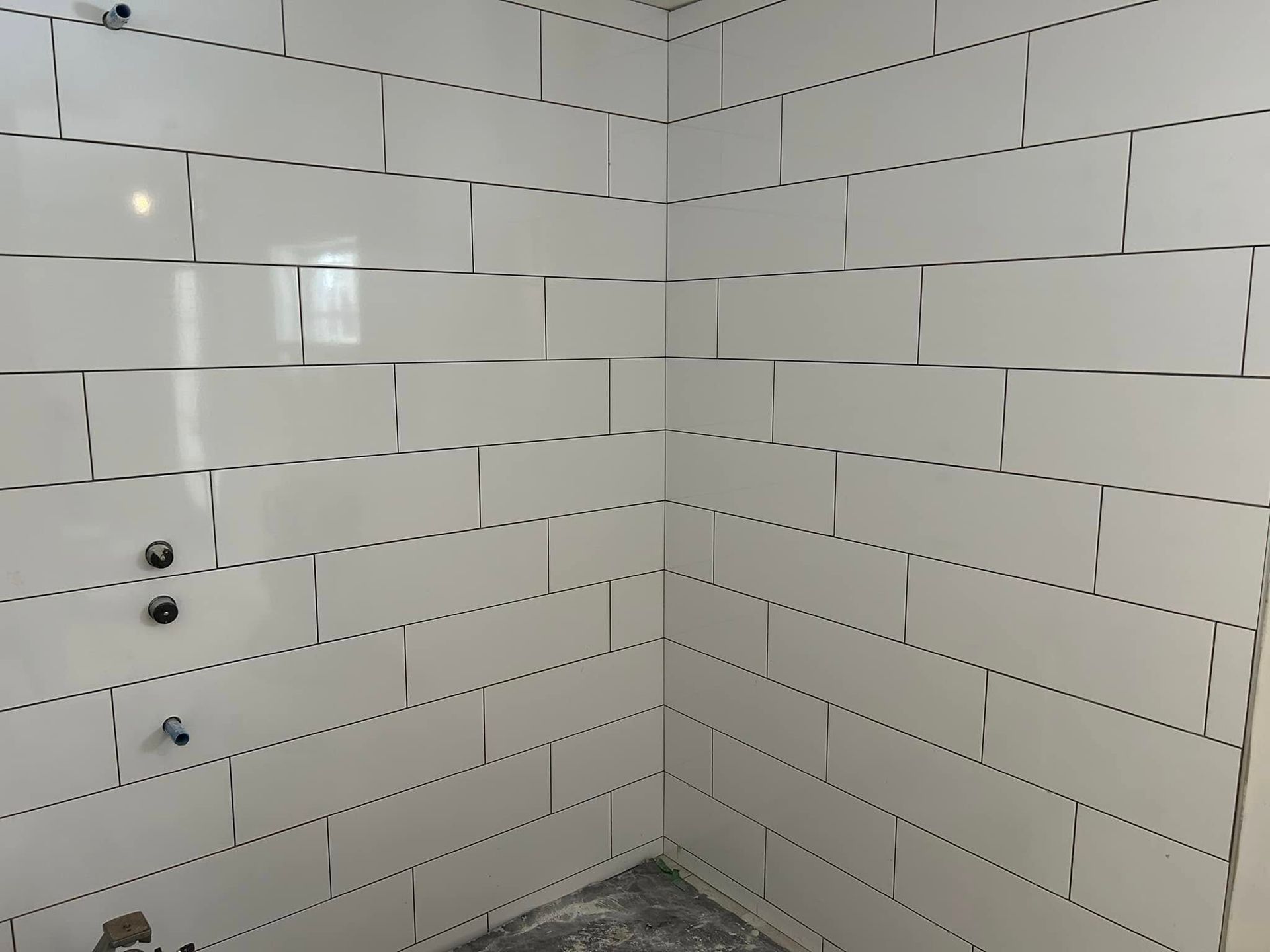 Une salle de bain avec du carrelage blanc aux murs et un sol gris.