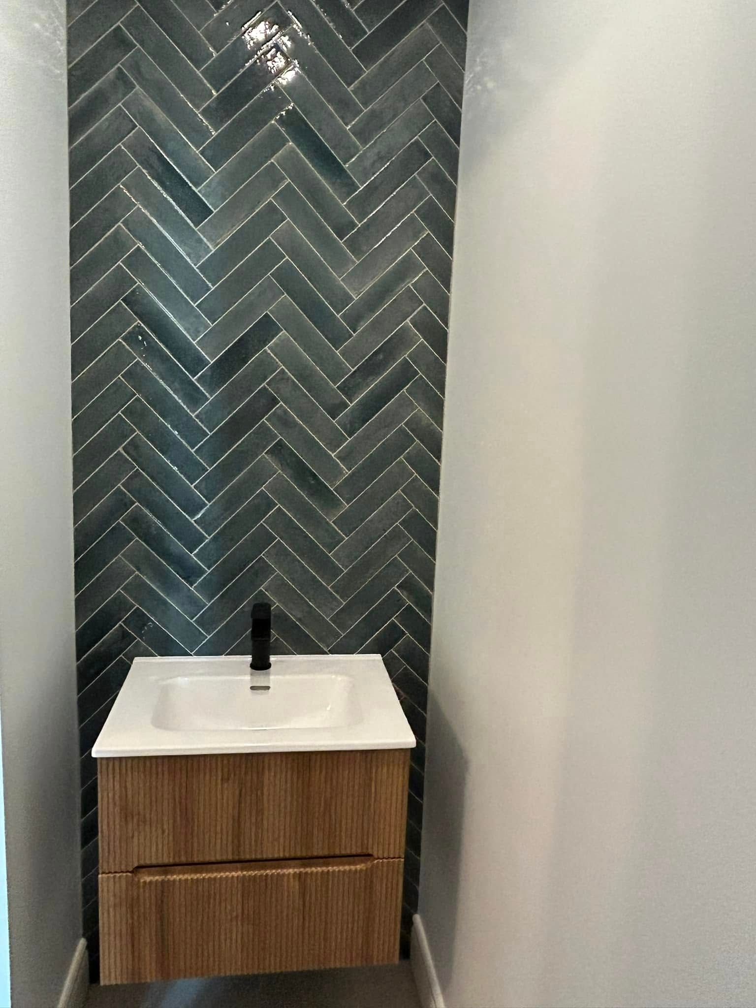 Une salle de bain avec un lavabo et un mur en carrelage à chevrons.