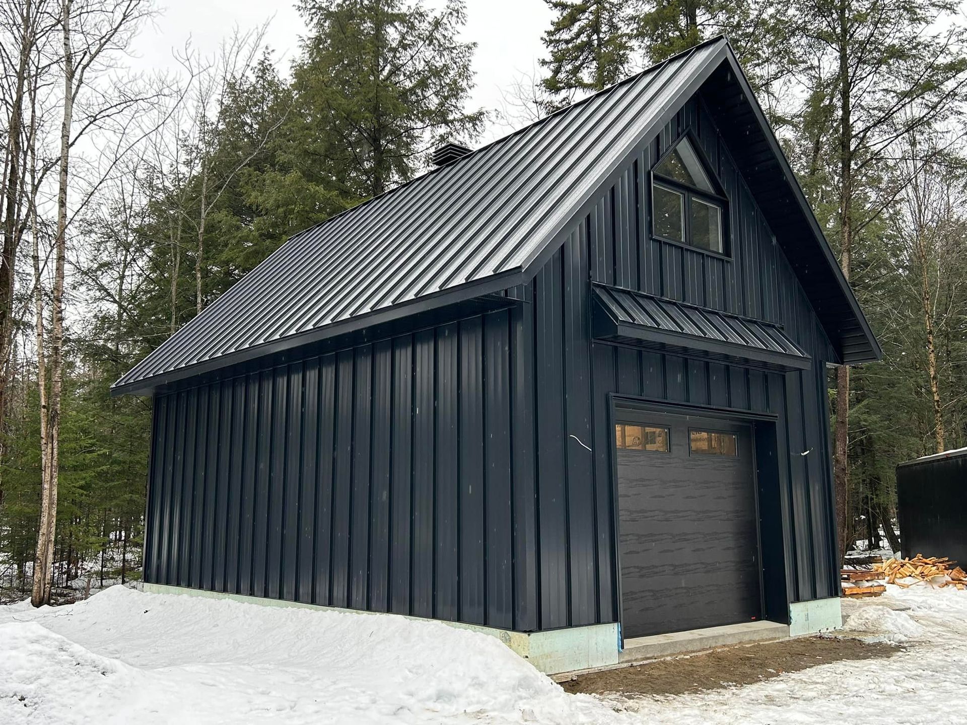 Un garage noir avec un toit en métal se trouve au sommet d'une colline couverte de neige.