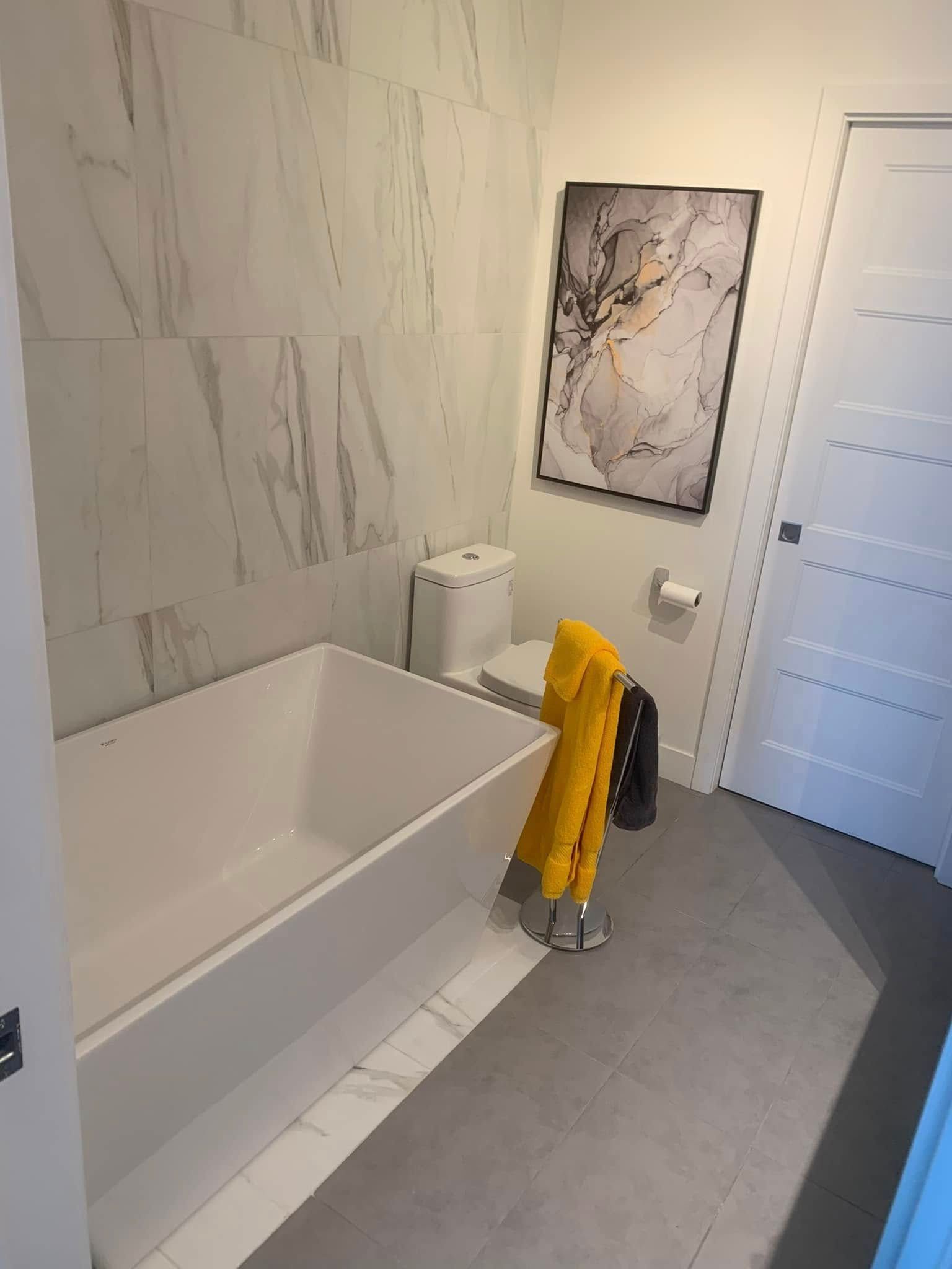 Une salle de bain avec baignoire, toilettes et tableau au mur.