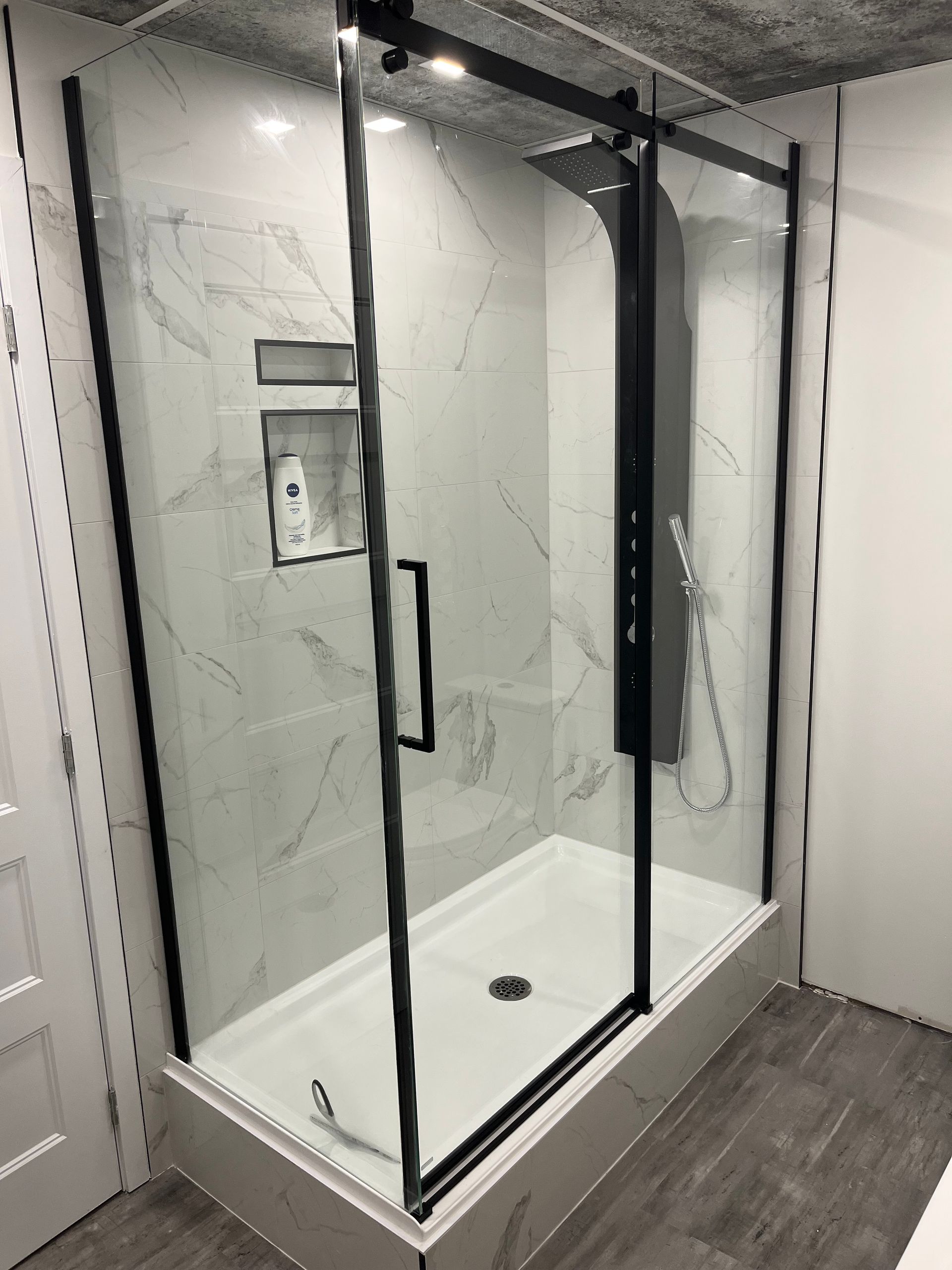 Une cabine de douche avec un cadre noir et des portes coulissantes en verre dans une salle de bain.
