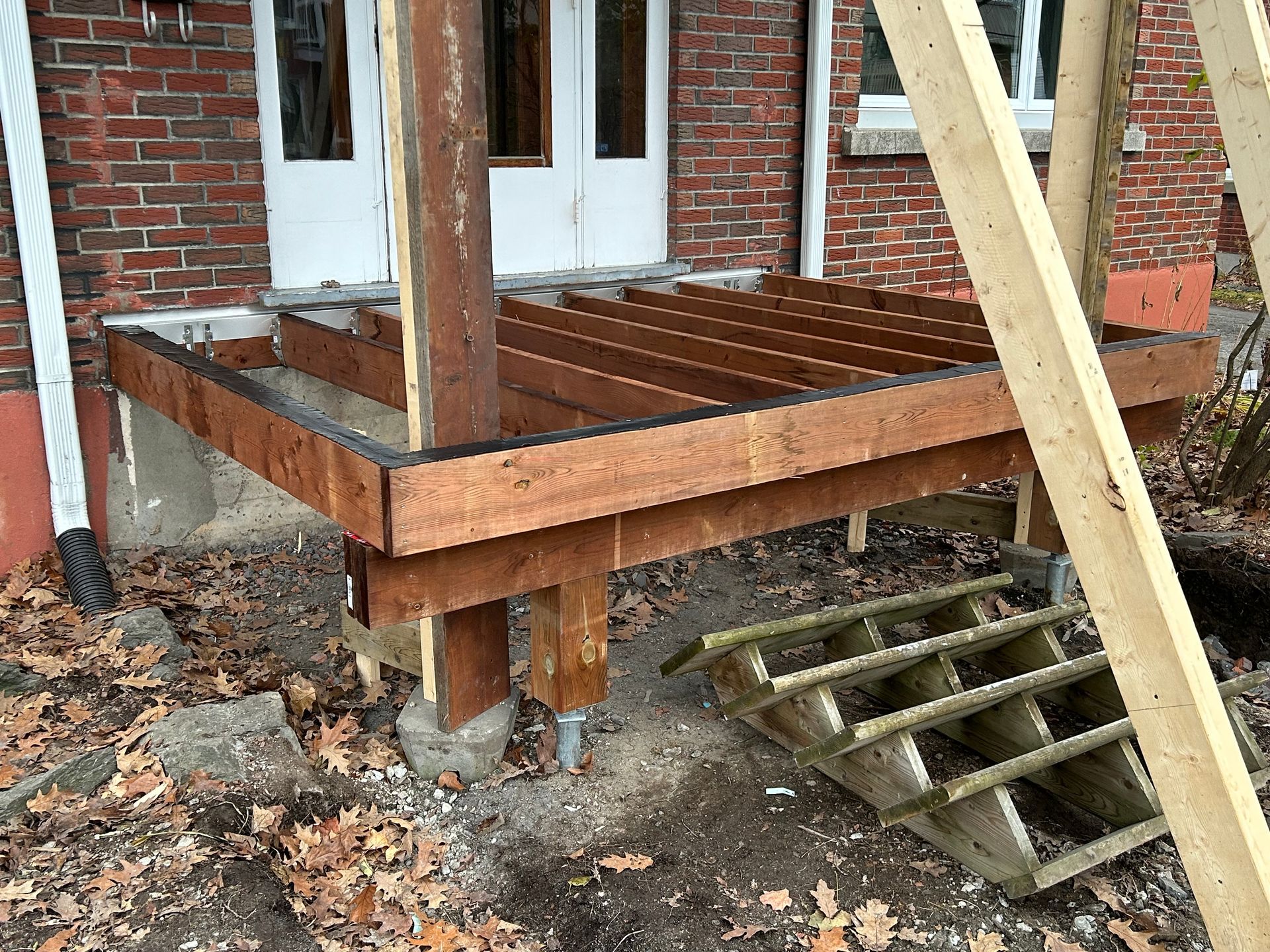 Une terrasse en bois est en cours de construction devant une maison en briques.