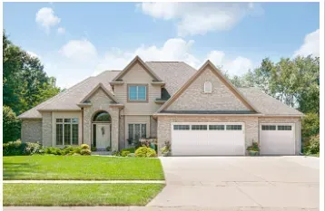 Suburban beige brick house with three-car garage, green lawn, and blue sky Suburban beige brick house with three-car garage, green lawn, and blue sky