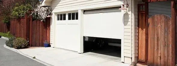 Residential garage with white door and a raised black opening beside a wooden fence on a driveway Residential garage with white door and a raised black opening beside a wooden fence on a driveway