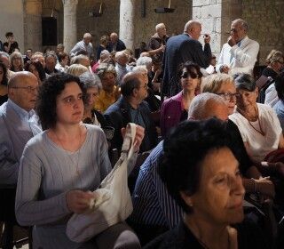 Un folto gruppo di persone è seduto in una stanza e assiste a un concerto