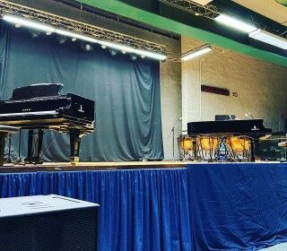 Un pianoforte è posizionato su un palco davanti a una tenda blu.