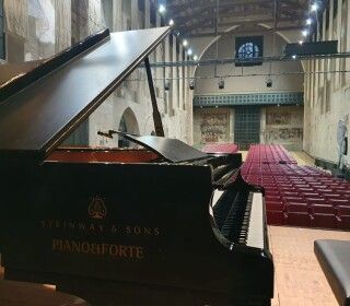 Un pianoforte è posizionato in un grande auditorium con sedili rossi.