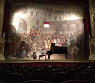 Un uomo sta suonando il pianoforte su un palco davanti a un grande dipinto.