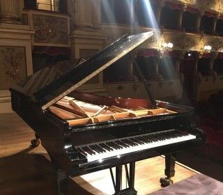 Un pianoforte a coda è posizionato sul palco di un teatro con il coperchio aperto.