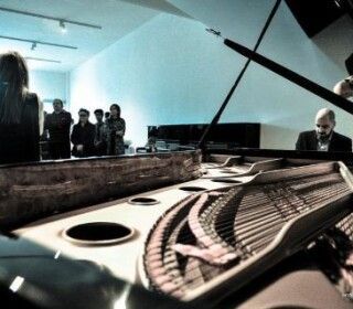 Un gruppo di persone è in piedi attorno a un pianoforte in una stanza.