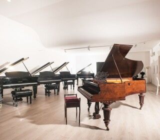 Un pianoforte è posizionato in una stanza circondato da altri pianoforti.