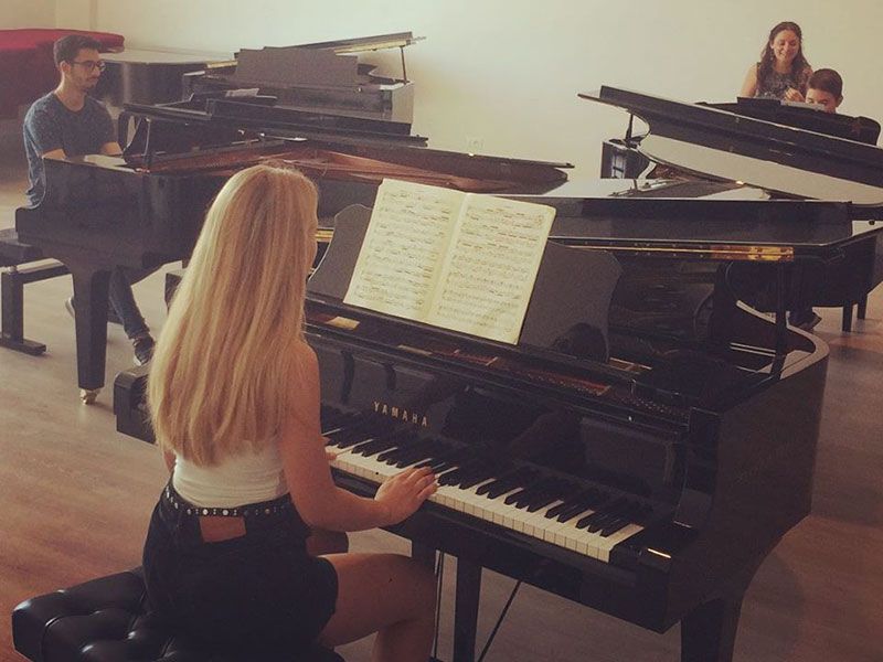 Una donna sta suonando il pianoforte in una stanza con altre persone che suonano il pianoforte