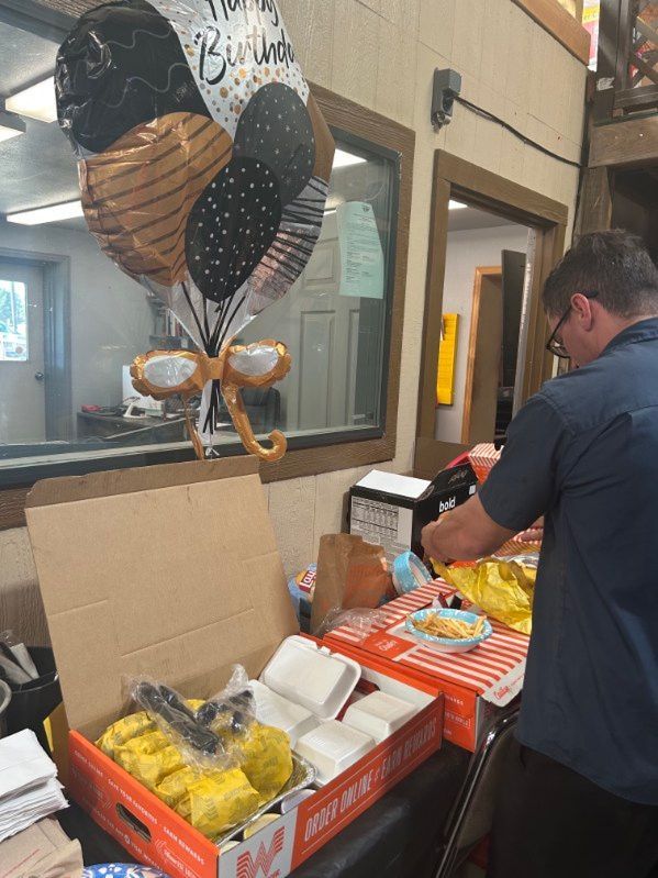 Person packing a donation box with balloons and food items in a store checkout area | Pete's Automotive