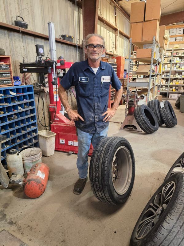 Mechanic standing in a tire shop beside loose tires and shelves of parts