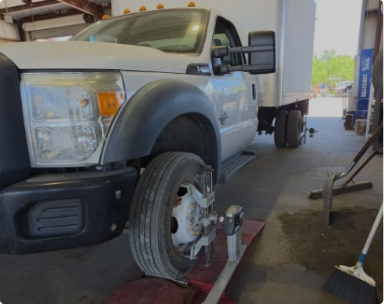 White pickup truck on a lift with front wheel removed in a garage, showing brake components. | Pete's Automotive