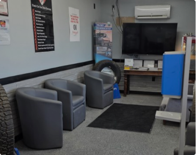 Small waiting room with gray chairs, a TV, wall-mounted AC, and a black rug. | Pete's Automotive