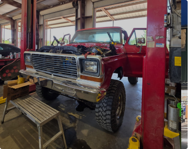 Red pickup truck with its hood open inside an auto repair shop on a lift. | Pete's Automotive