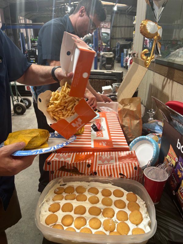 Food stall worker pouring noodles into a tray beside a box of egg tarts on a counter. | Pete's Automotive