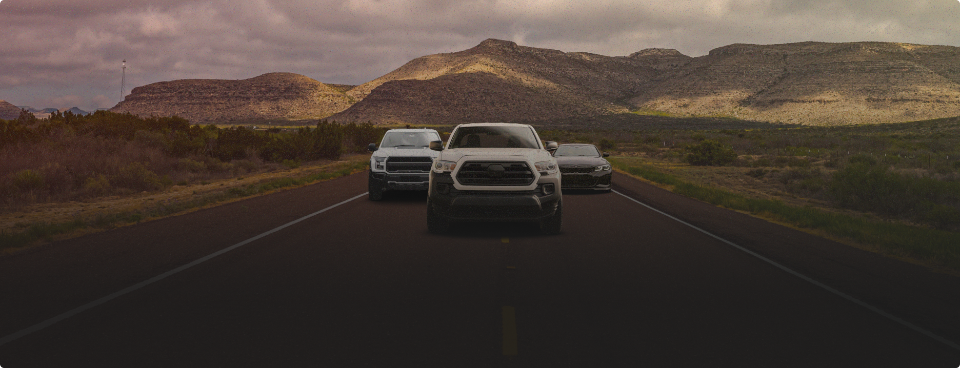 Three cars driving on a desert highway toward rocky hills at dusk | Pete's Automotive