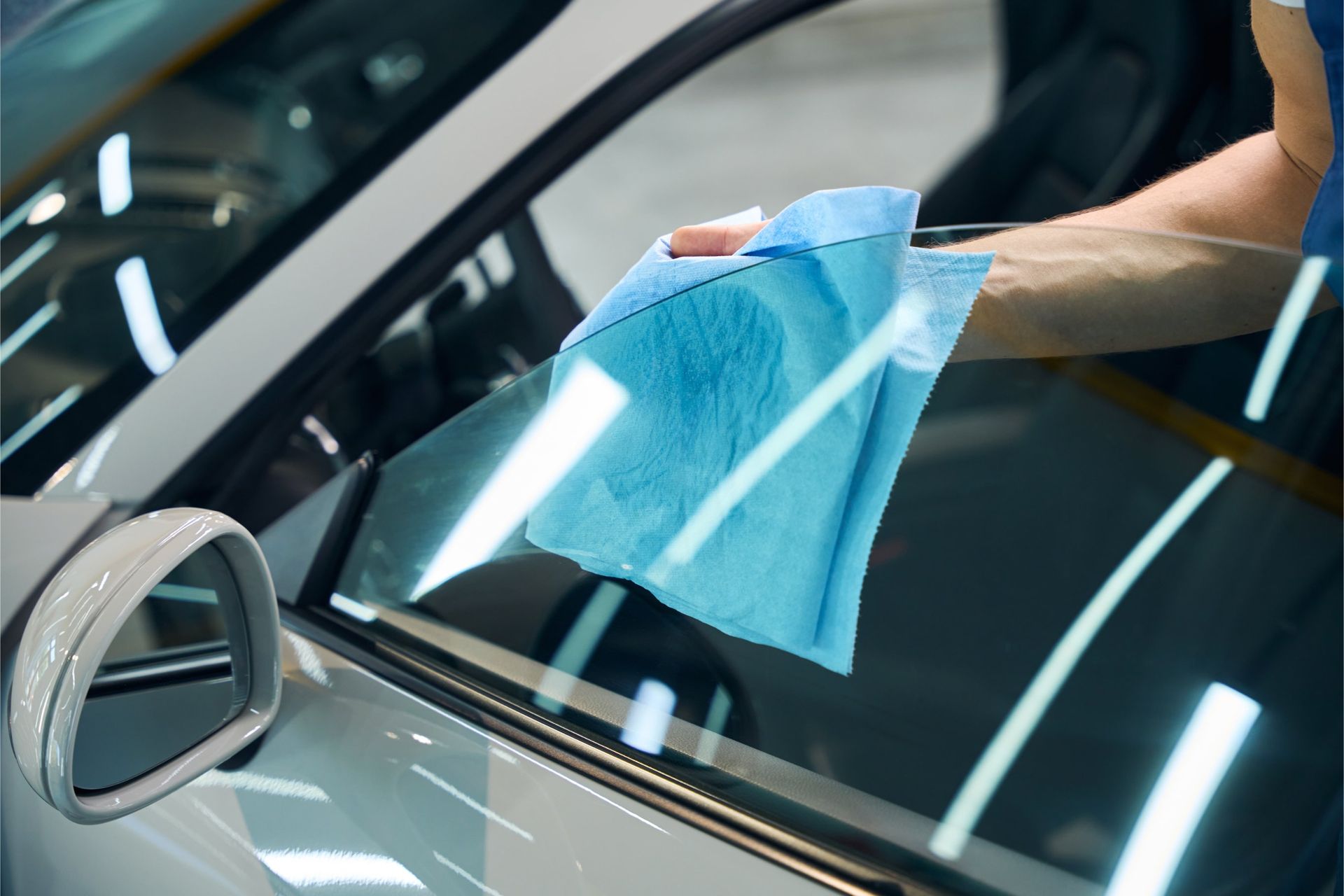 A person wiping the glass of a car window with a blue cloth in a garage.
