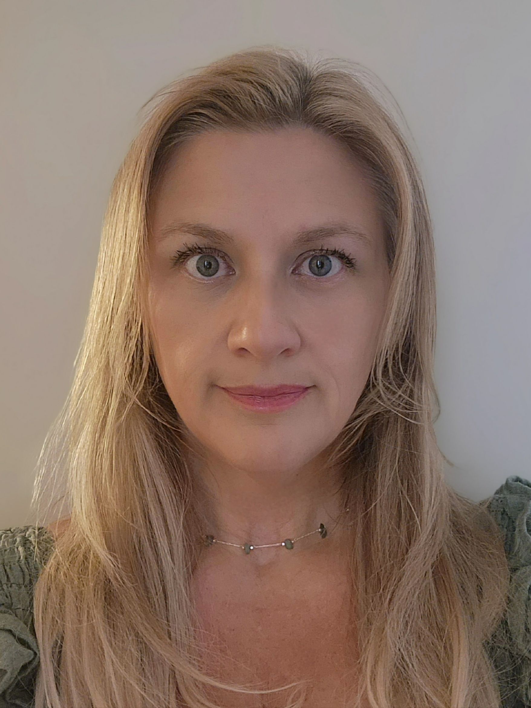 A woman with blonde hair is wearing a black shirt and a necklace.