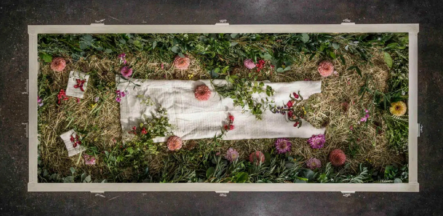 A photo over a casket with flowers and natural decomposition for terramation