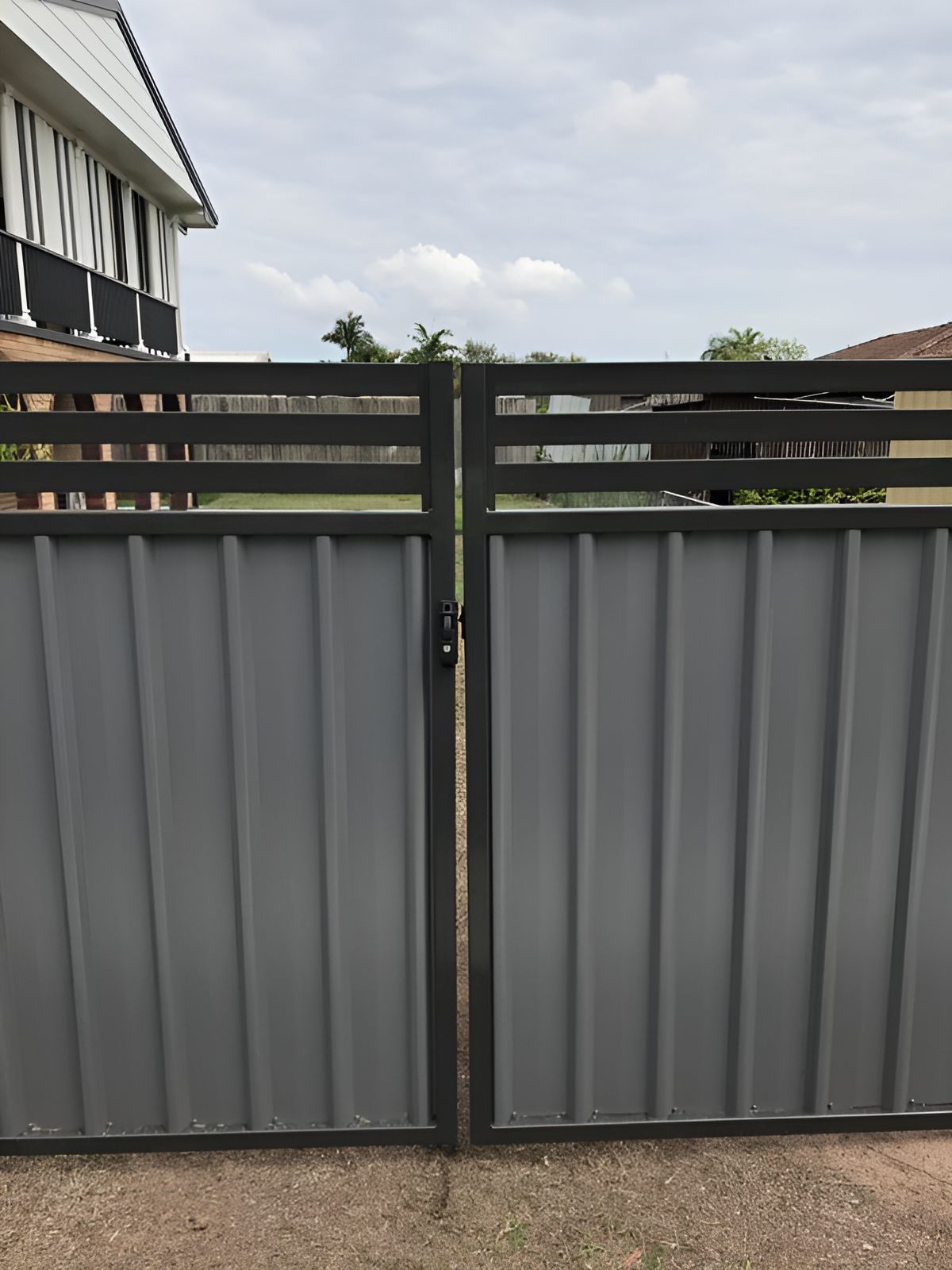 A Grey Metal Gate With a Black Frame is Sitting in Front of a House — DC Fencing In Wondunna, QLD